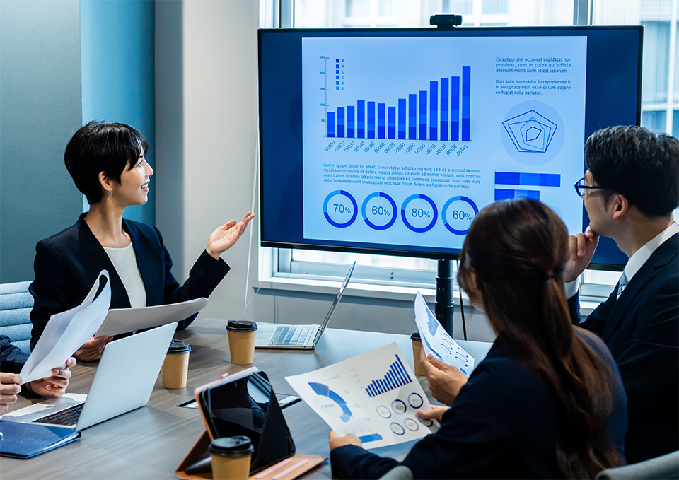モニターのデータを見て議論するビジネスチームメンバーたちの様子の画像